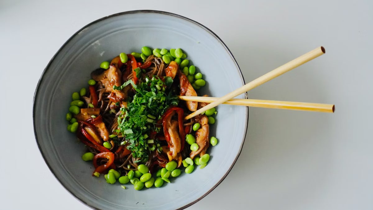 Top view of a vibrant Asian salad with edamame and noodles in a ceramic bowl.